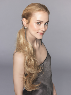 Vrouw draagt het Champagne haarstuk van Ellen Wille – lange, golvende wrap-around paardenstaart in een natuurlijke blondtint met elegante uitstraling.